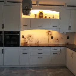 Nowoczesna, biała kuchnia na wymiar z ciemnym blatem i panelem szklanym z motywem dmuchawców, oświetlona listwą LED i wyposażona w zabudowane sprzęty AGD.