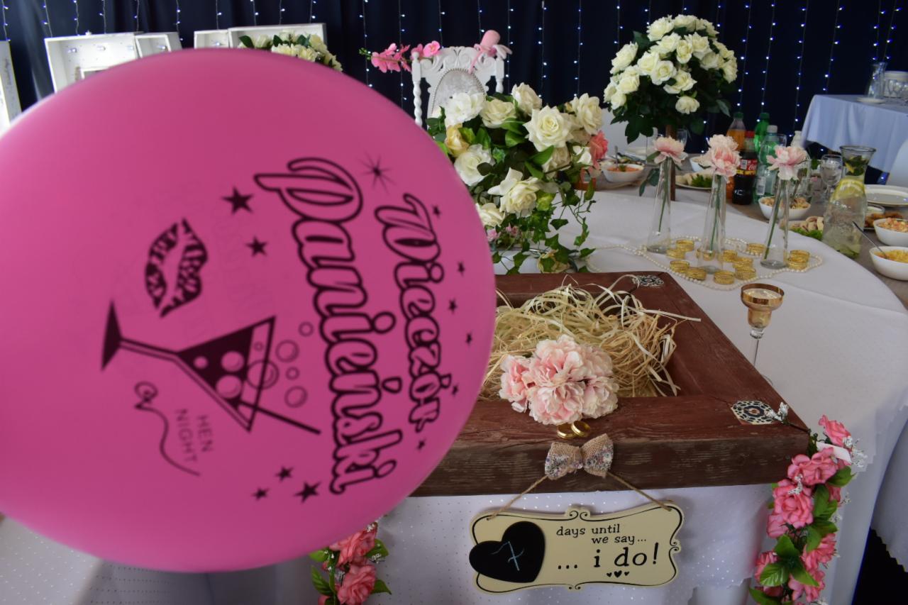 Dekoracja stołu na wieczór panieński z różowym balonem z napisem 'Wieczór Panieński', kwiatami, drewnianą ramką z sianem i tabliczką z napisem 'days until we say... I do!'