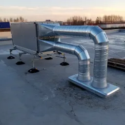 System wentylacji mechanicznej z rekuperacją na dachu budynku, widoczne metalowe kanały wentylacyjne i centrala, montaż na konstrukcji wsporczej z gumowymi podkładkami antywibracyjnymi.