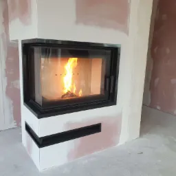 Nowoczesny wkład z szybą, obudowany białą konstrukcją z czarnymi akcentami, w trakcie prac wykończeniowych pomieszczenia.