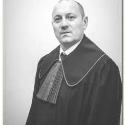 Portret mężczyzny w todze adwokackiej na jasnym tle, z delikatnym uśmiechem i widoczną fakturą materiału togi.