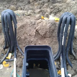 Podłączenie rur w ziemi do czarnej skrzynki, widoczne zabezpieczenia i elementy instalacji.