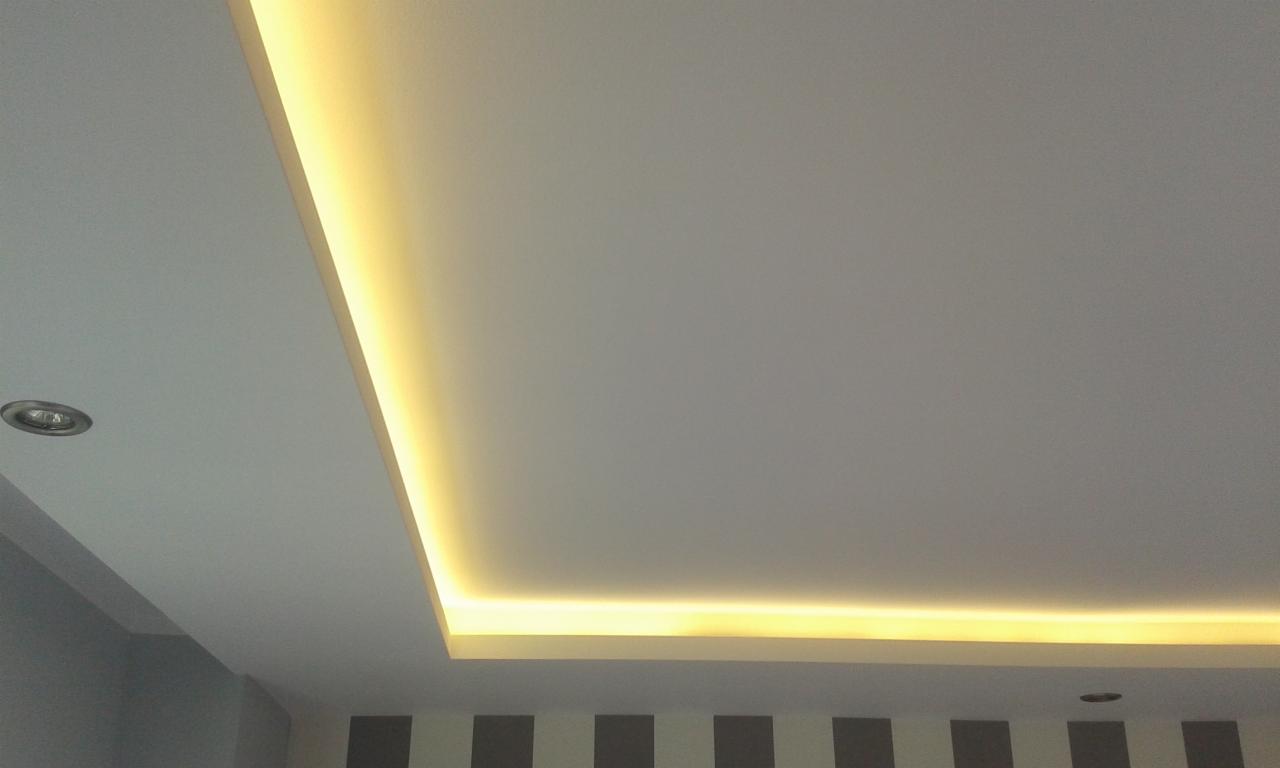 Podwieszany sufit z oświetleniem LED w narożniku, widoczny fragment ściany w pasy.