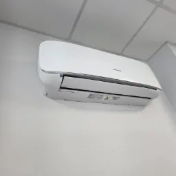 Biała klimatyzacja Hisense zamontowana na ścianie w pomieszczeniu z kasetonowym sufitem. Widok z dołu, lekki kąt.