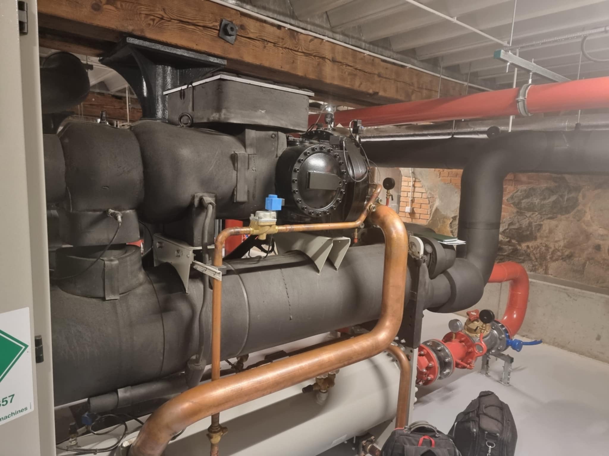 Duża przemysłowa instalacja chłodnicza z rurami miedzianymi i czerwonymi, zamontowana w pomieszczeniu z ceglanym murem w tle.