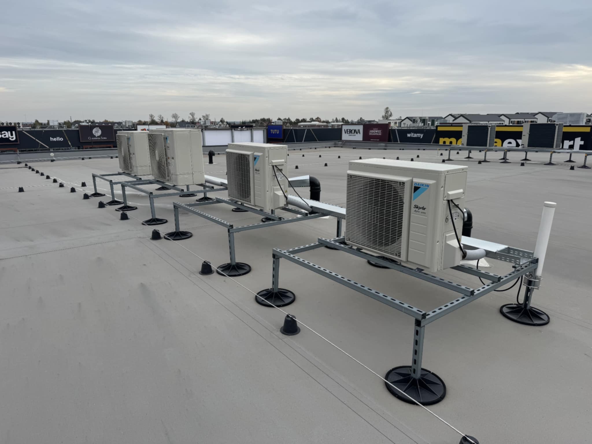 Instalacja klimatyzacji Daikin SkyAir na dachu budynku. Cztery jednostki zewnętrzne na metalowych konstrukcjach, z widocznymi przewodami i elementami montażowymi.