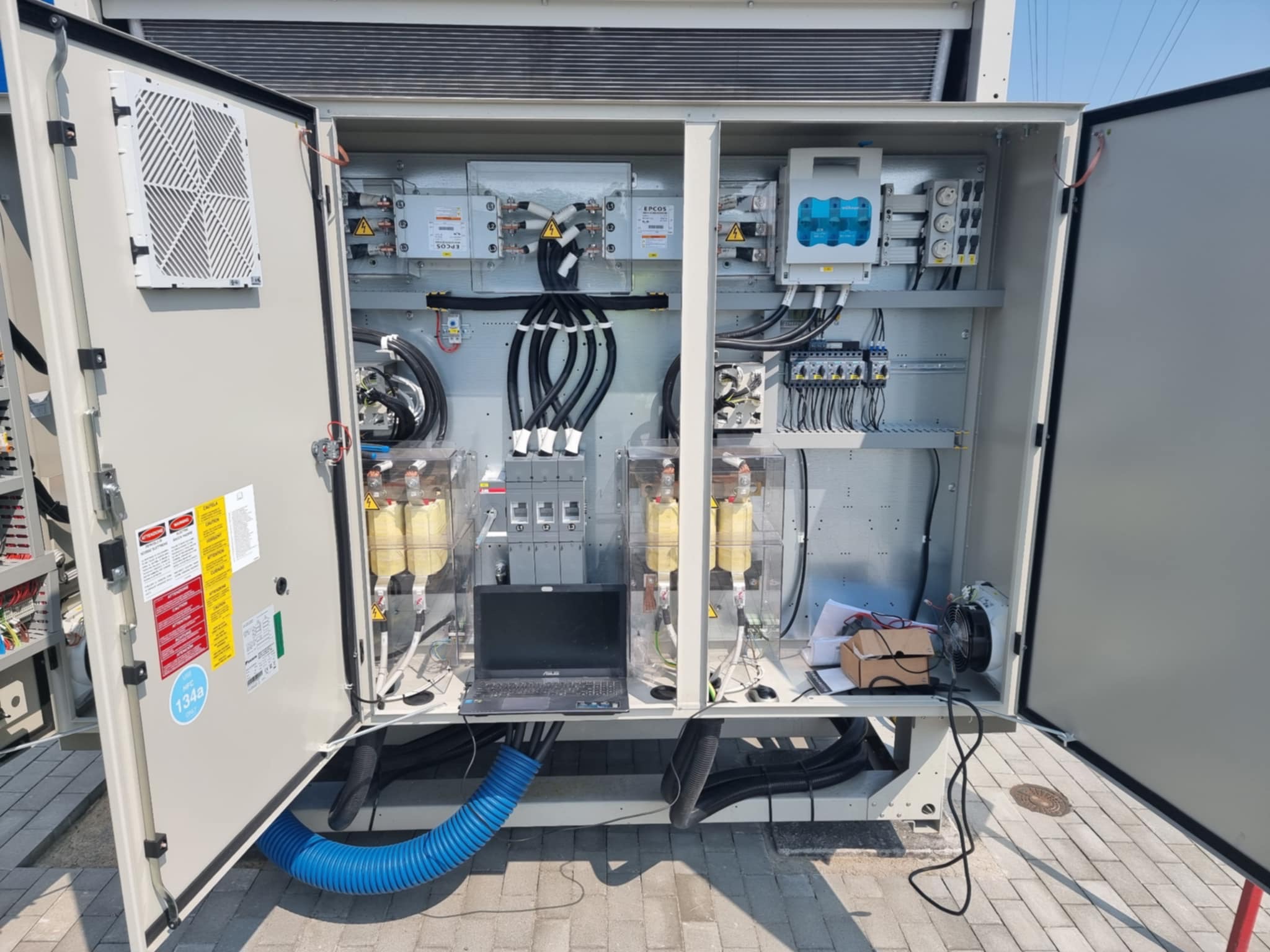 Otwarta szafa sterownicza z laptopem w środku, widoczne kable, bezpieczniki i inne elementy elektryczne. Diagnostyka i serwis klimatyzacji przemysłowej.