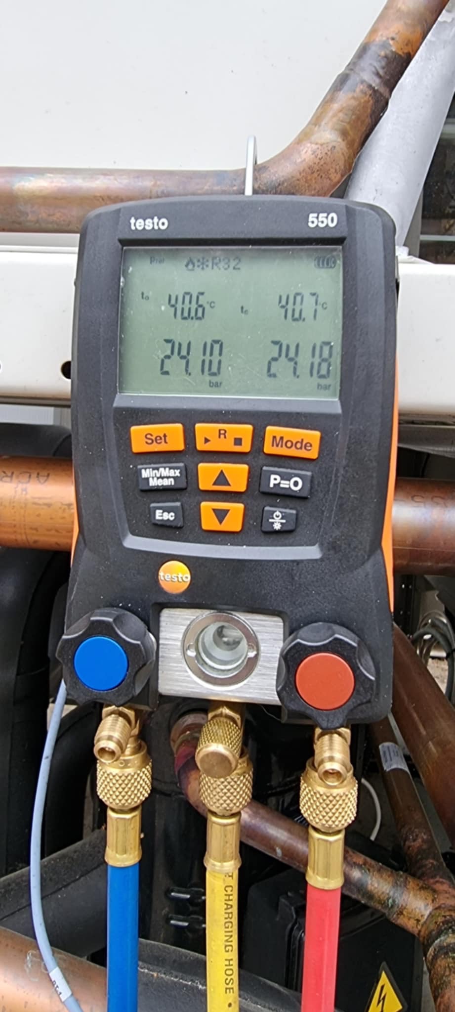 Miernik Testo 550 podłączony do instalacji chłodniczej, wskazujący temperaturę i ciśnienie czynnika R32. Widoczne przewody, zawory i fragment instalacji.