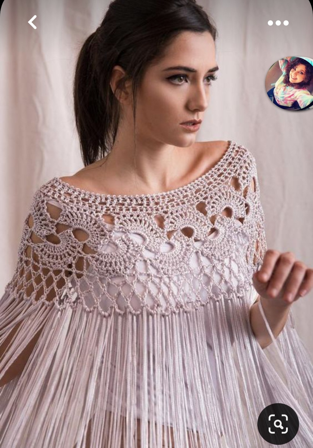 Portret kobiety w ażurowym, ręcznie robionym bolerku z frędzlami, w odcieniach beżu i bieli, na tle jasnej tkaniny.