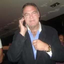 Mężczyzna w marynarce rozmawia przez telefon, poprawiając koszulę i prezentując złoty zegarek na nadgarstku.