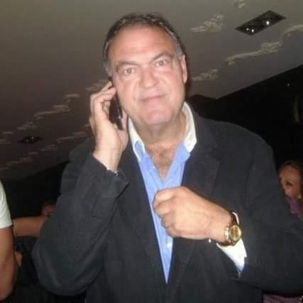 Mężczyzna w marynarce rozmawia przez telefon, poprawiając koszulę i prezentując złoty zegarek na nadgarstku.