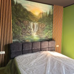 KARLITO WYKOŃCZENIA WNĘTRZ ADRIAN GŁUSZCZAK - Sypialnia po remoncie: łóżko z szarą ramą, ściana z malowidłem wodospadu otoczona drewnianymi lamelami. Zielona ściana w tle. Nowoczesny design.