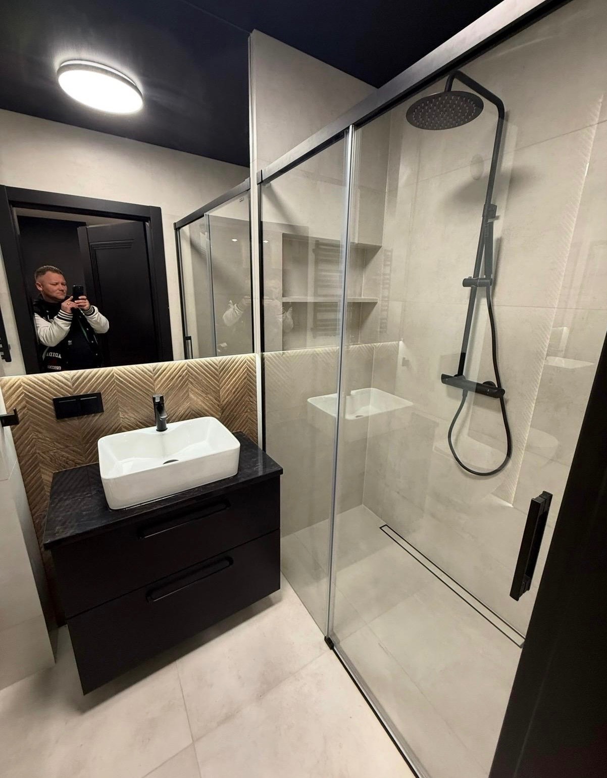 Nowoczesna łazienka z kabiną prysznicową typu walk-in i umywalką nablatową w Gorzowie Wielkopolskim. Czarna armatura i drewnopodobna ściana dodają elegancji.