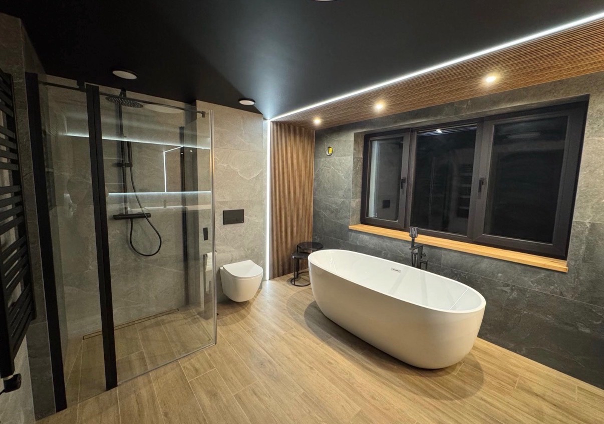 Nowoczesna łazienka z kabiną prysznicową typu walk-in, wolnostojącą wanną i drewnianymi akcentami na suficie i ścianie. Użyto szarych płytek imitujących kamień.