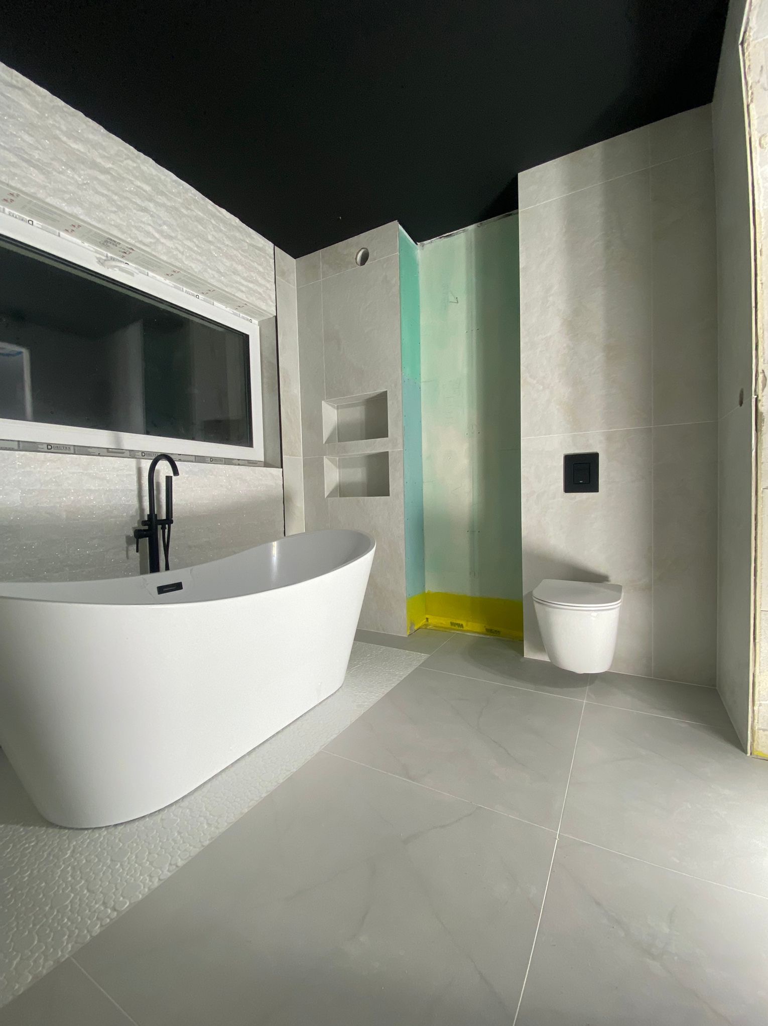 Nowoczesna łazienka w Gorzowie Wielkopolskim z wolnostojącą wanną, podwieszaną toaletą i szarą glazurą. Widoczne przygotowania do montażu kabiny prysznicowej.