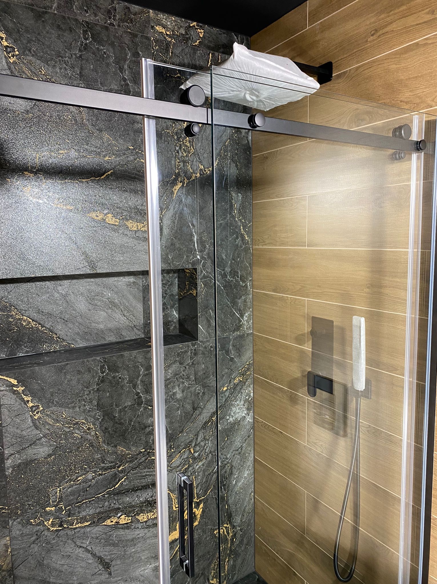 Kabina prysznicowa z przesuwnymi drzwiami i czarnymi okuciami, wykończona płytkami imitującymi drewno i marmur w Gorzowie Wielkopolskim.