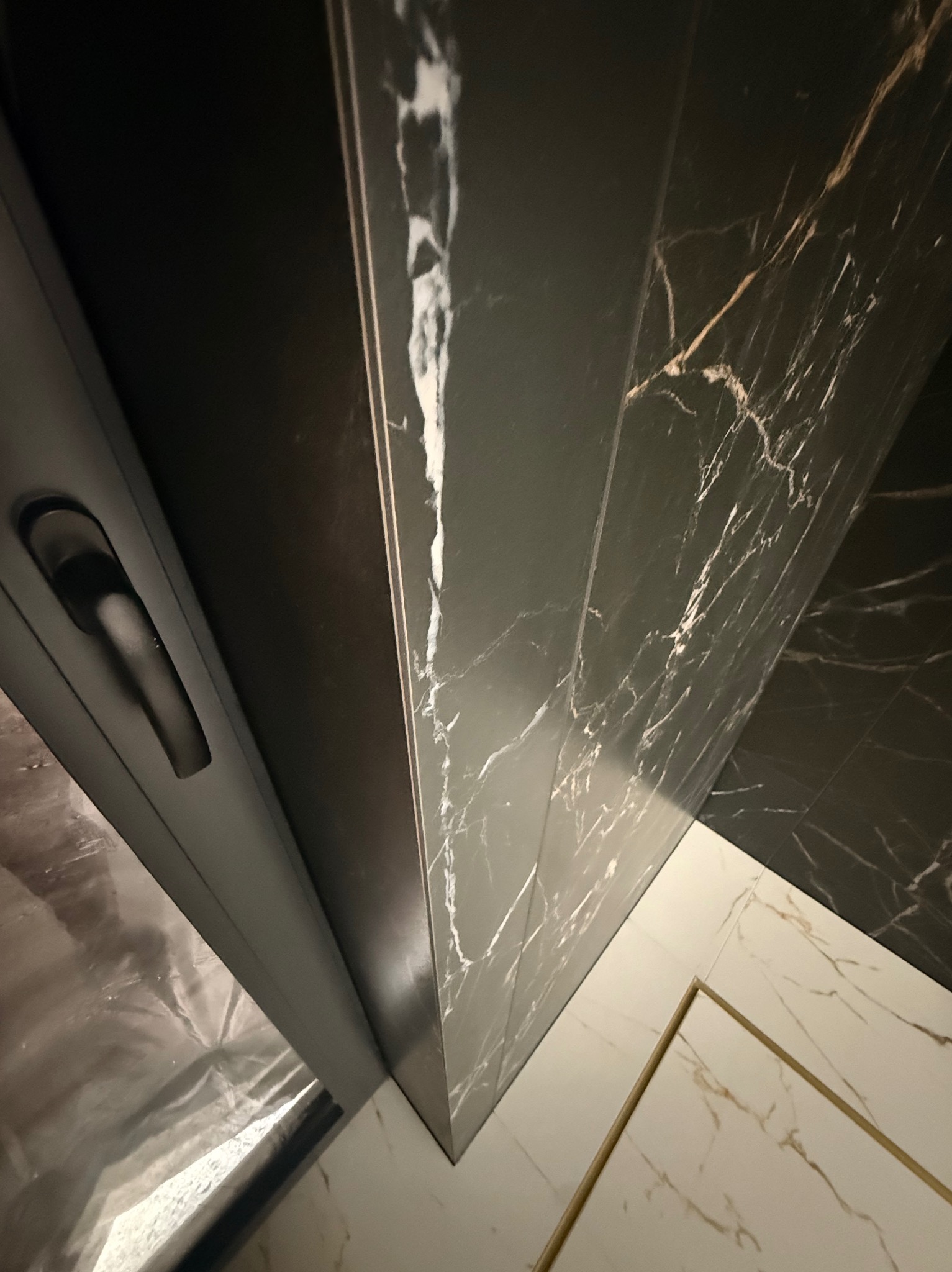 Częściowy widok wykończonej łazienki z czarnymi płytkami imitującymi marmur na ścianie i białymi na podłodze, widoczna kabina prysznicowa z czarną ramą.