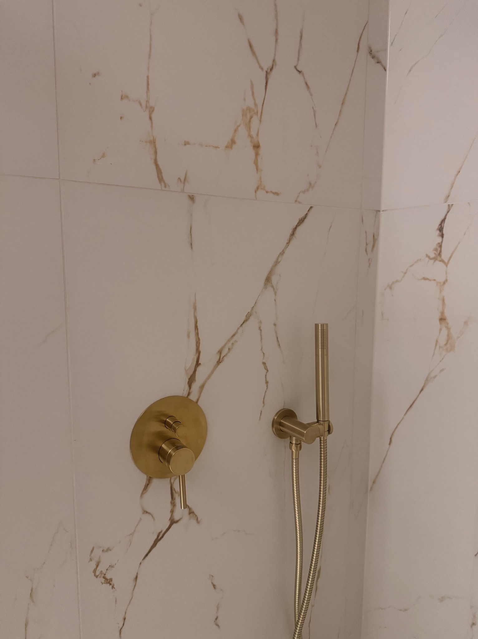 Bateria prysznicowa w kolorze złotym na tle białych płytek imitujących marmur. Nowoczesna łazienka po remoncie, detale wykończenia.