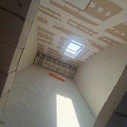 Wykończenia Wnętrz Karol Wysocki - Wnętrze w trakcie wykończenia w Mońkach: ściany po szpachlowaniu, widoczne profile pod płyty gipsowe na suficie ze świetlikiem, przygotowane do dalszych prac.