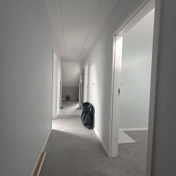 Wykończenia Wnętrz Karol Wysocki - Korytarz w szarościach po remoncie: świeżo pomalowane ściany, szara podłoga, widoczny właz na strych i worek z odpadami. Minimalistyczne wykończenie wnętrza.