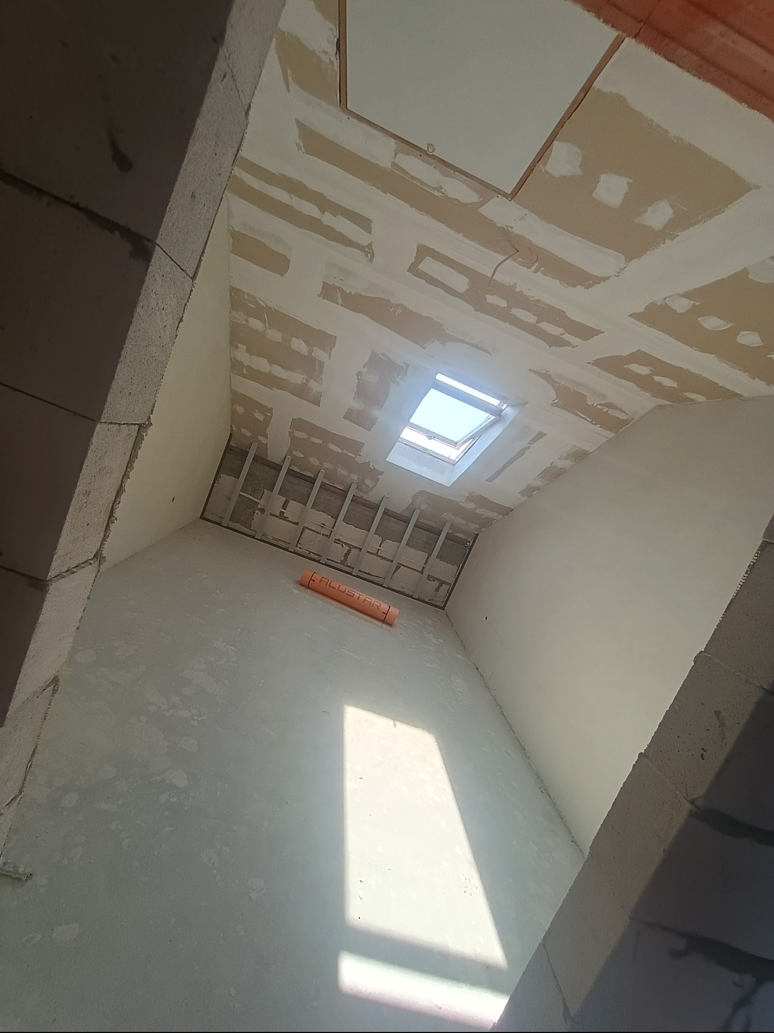 Wnętrze w trakcie wykończenia w Mońkach: ściany po szpachlowaniu, widoczne profile pod płyty gipsowe na suficie ze świetlikiem, przygotowane do dalszych prac.