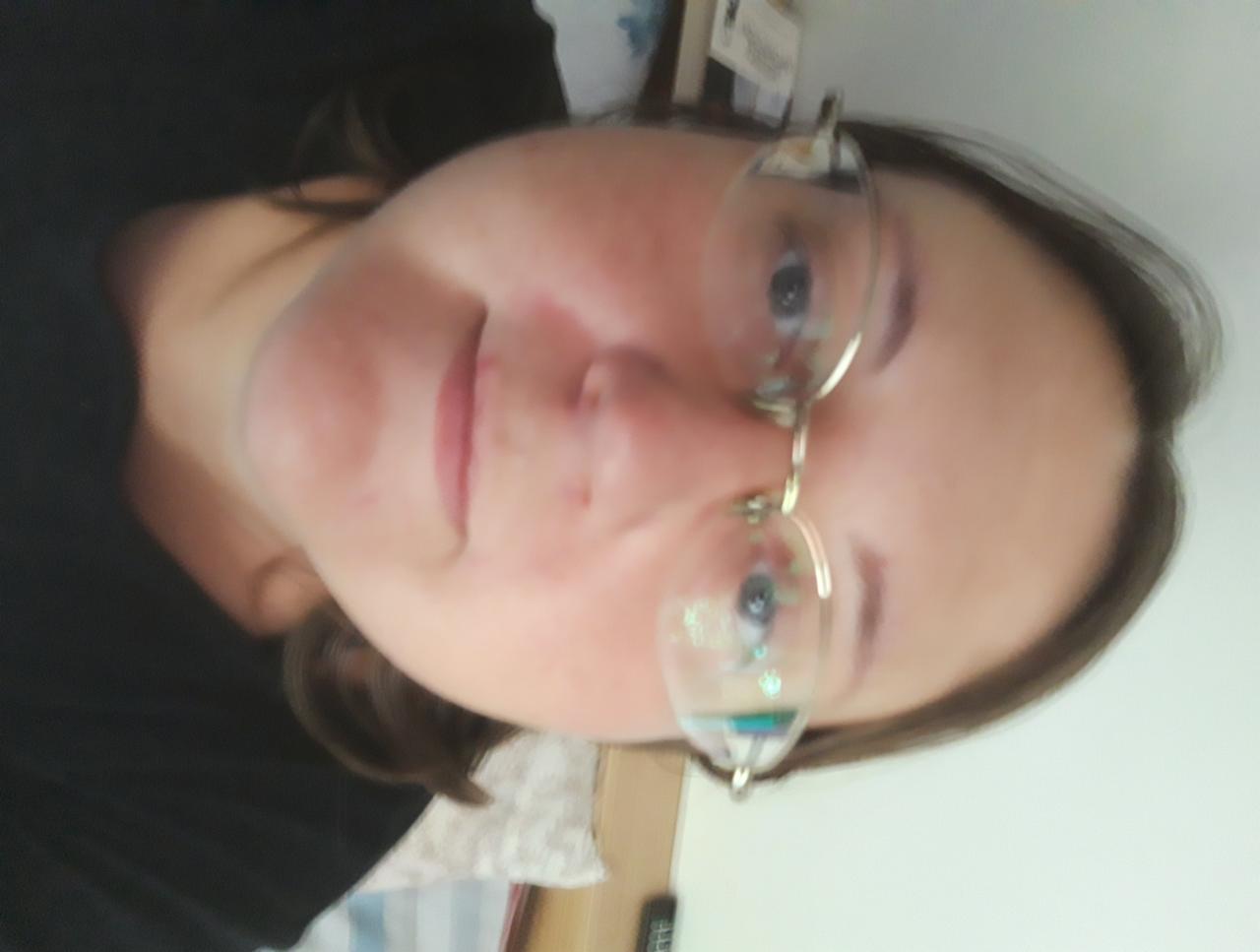 Portret kobiety w okularach z zawieszkami, ujęcie z dołu, obrócone o 90 stopni. Widoczne odbicia w szklach.