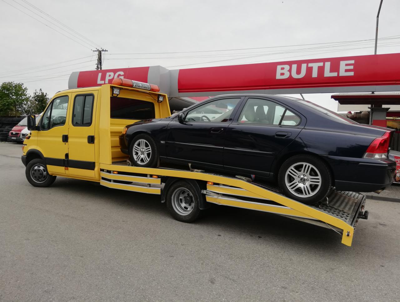 Żółta ciężarówka pomocy drogowej z niebieskim Volvo na platformie, na tle stacji benzynowej w Puławach.