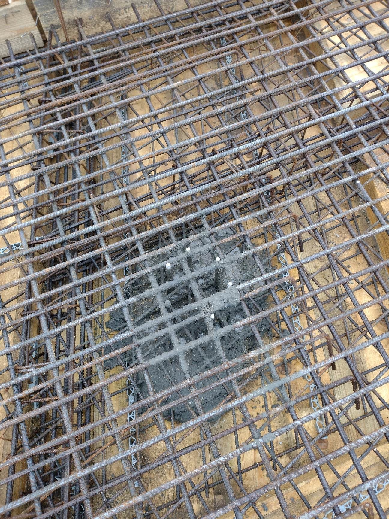 Siatka zbrojeniowa z betonu na drewnianym szalunku, widoczne spoiwa z tworzywa sztucznego.