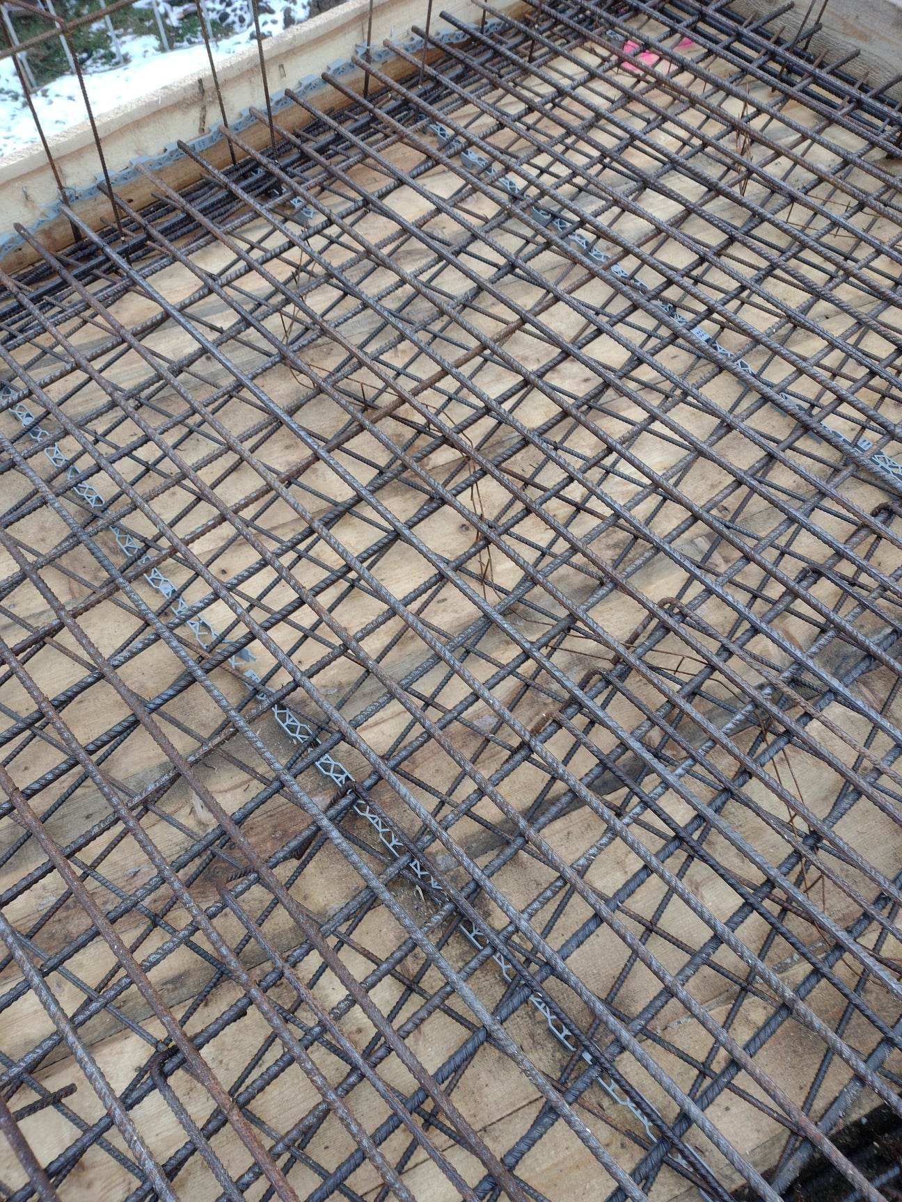 Siatka zbrojeniowa ułożona na deskach szalunkowych, widoczne dystanse z tworzywa sztucznego, przygotowanie do wylewki fundamentów.