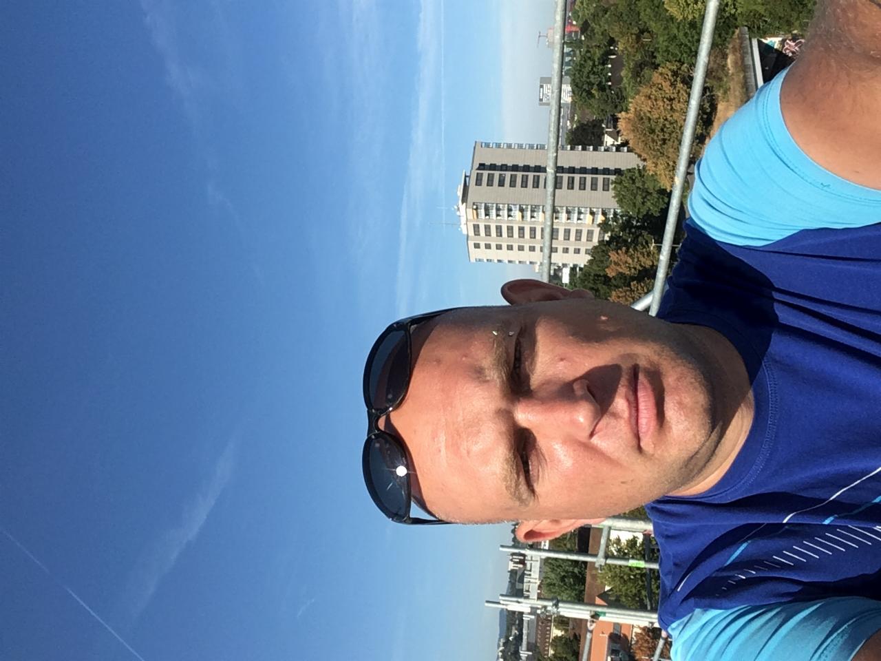 Autoportret mężczyzny w okularach na tle błękitnego nieba i miejskiego krajobrazu z rusztowaniem. Ujęcie z dołu.