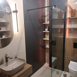 BIMAR Mariusz Bielecki - Nowoczesna łazienka z umywalką nablatową, kabiną prysznicową typu walk-in z czarnymi profilami i płytkami imitującymi drewno oraz pionowymi panelami ściennymi w kolorze grafitowym.