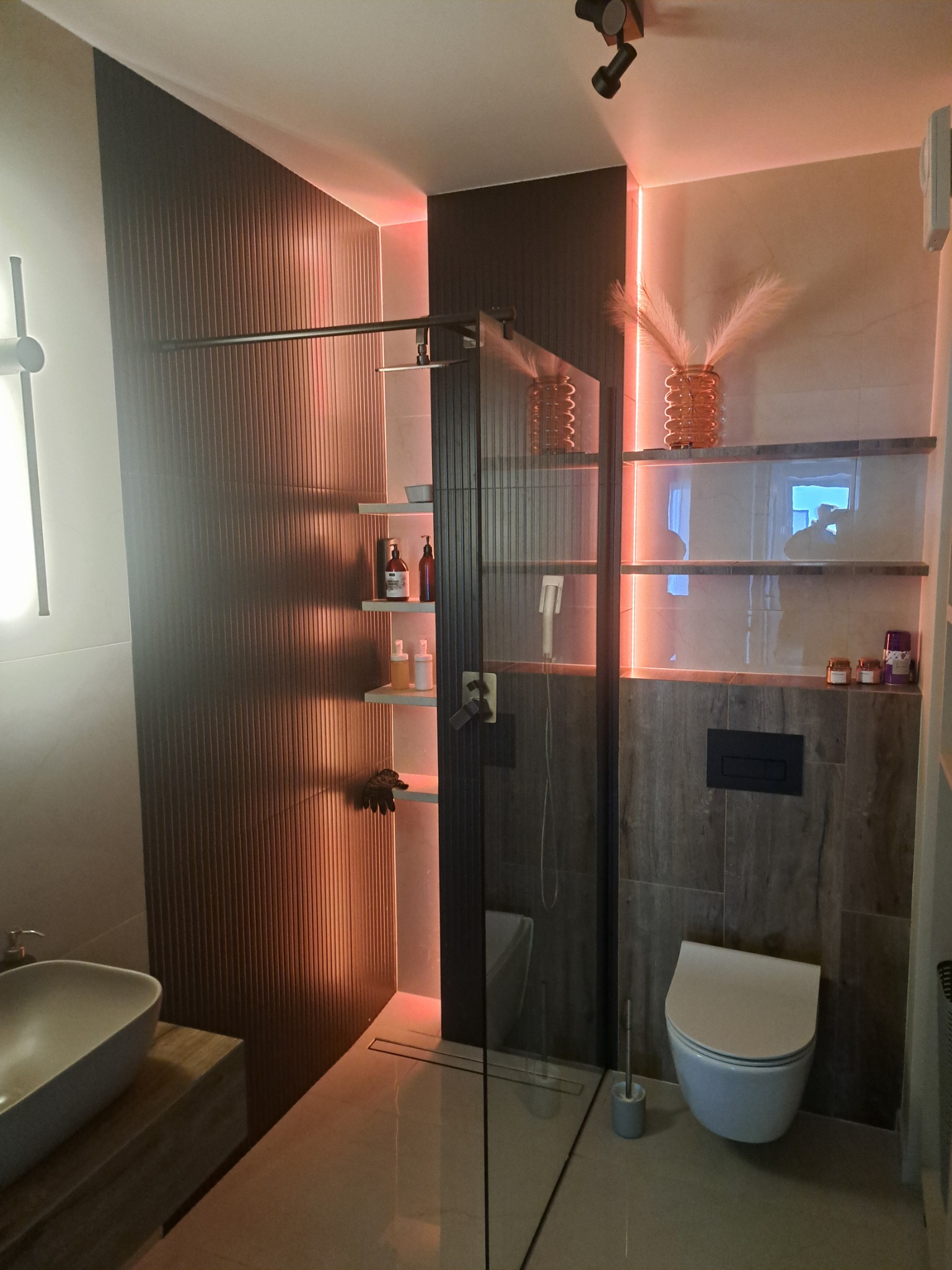 Nowoczesna łazienka z prysznicem typu walk-in, podświetlanymi półkami i umywalką nablatową, oświetlenie LED w ciepłych barwach.