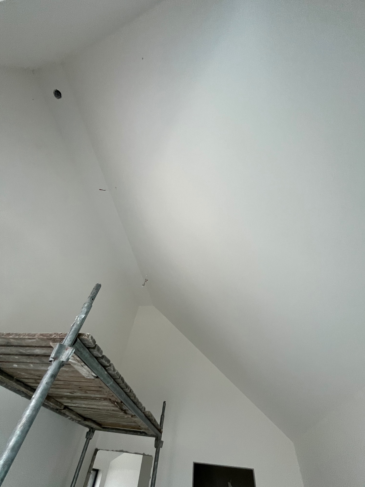 Świeżo pomalowane, białe poddasze ze skosami, widoczne ślady po szpachlowaniu i punktowe oświetlenie, częściowo zasłonięte przez metalowe rusztowanie.