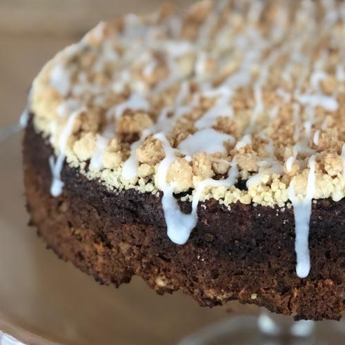 Ciemne ciasto z kruszonką i lukrem, widoczne z bliska z boku, na szklanej podstawie.