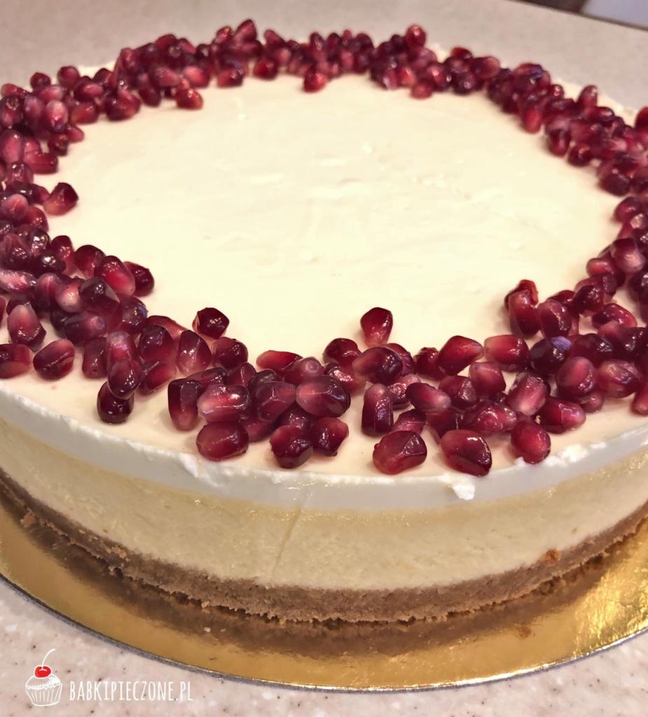 Okrągły sernik na złotym podkładzie, udekorowany obwódką z intensywnie czerwonych pestek granatu.