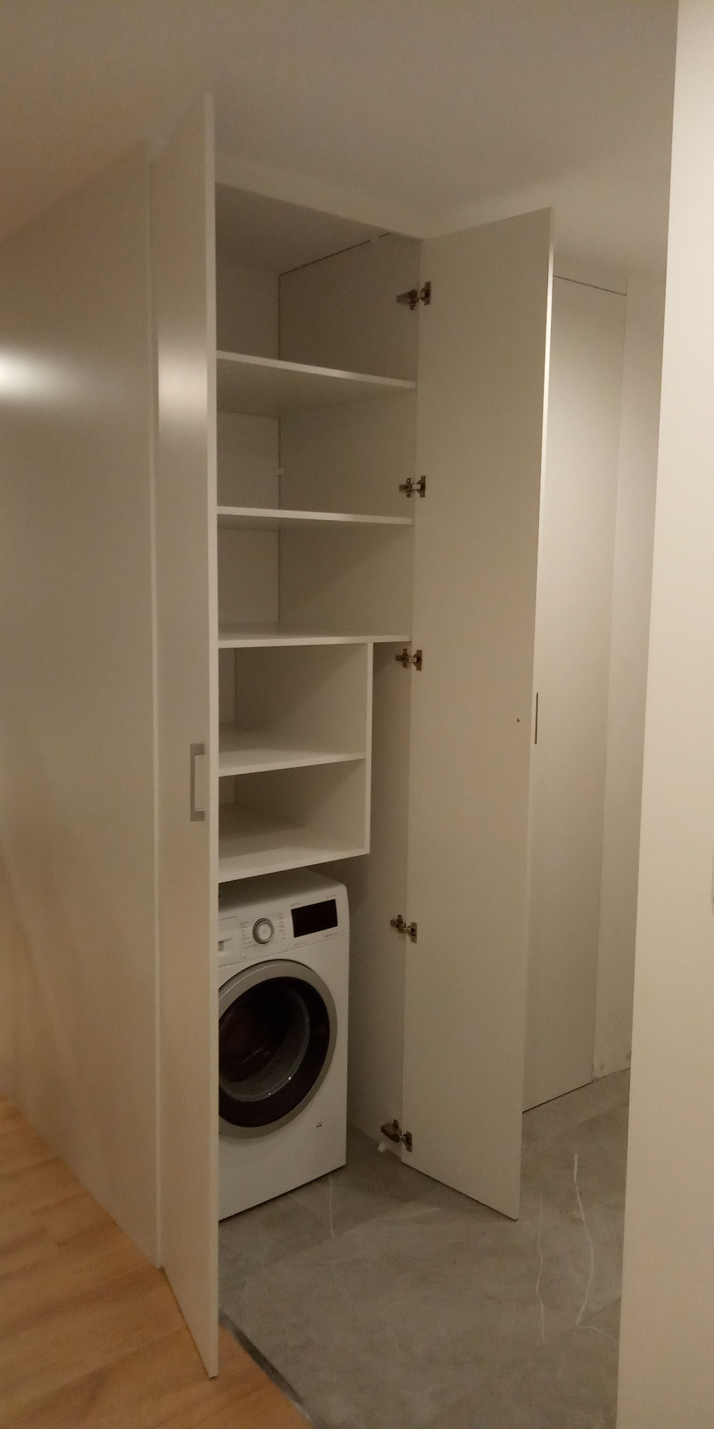Biała szafa wnękowa z otwartymi drzwiami, w której znajduje się pralka i półki.