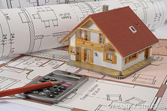 Model domu z czerwonym dachem umieszczony na planach architektonicznych z kalkulatorem i ołówkiem w tle, prezentujący projekt budowlany.
