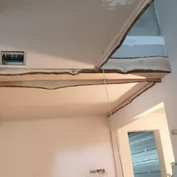 Sufit podwieszany z płyty gipsowo-kartonowej w trakcie montażu, widoczne profile i szpachlowane łączenia, surowy stan wykończenia ścian i widoczne przewody elektryczne.