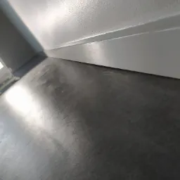 Świeżo pomalowana, gładka, szara ściana z listwą przypodłogową i szara podłoga z połyskiem, widok z dołu pod kątem.