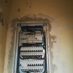 Rozdzielnica elektryczna z zabezpieczeniami i okablowaniem, zamontowana w ścianie w trakcie remontu, widoczne ślady po skuciu tynku.
