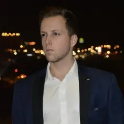 Portret mężczyzny w marynarce na tle nocnego miasta z rozmytymi światłami.