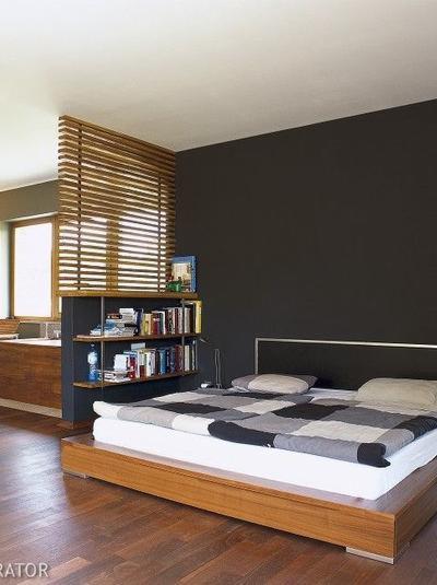 Nowoczesna sypialnia z drewnianą podłogą, łóżkiem z patchworkową narzutą i regałem z książkami oddzielającym przestrzeń.
