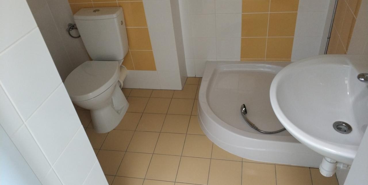 Umywalka, brodzik i toaleta w łazience z beżowymi płytkami podłogowymi i żółto-białymi płytkami ściennymi.