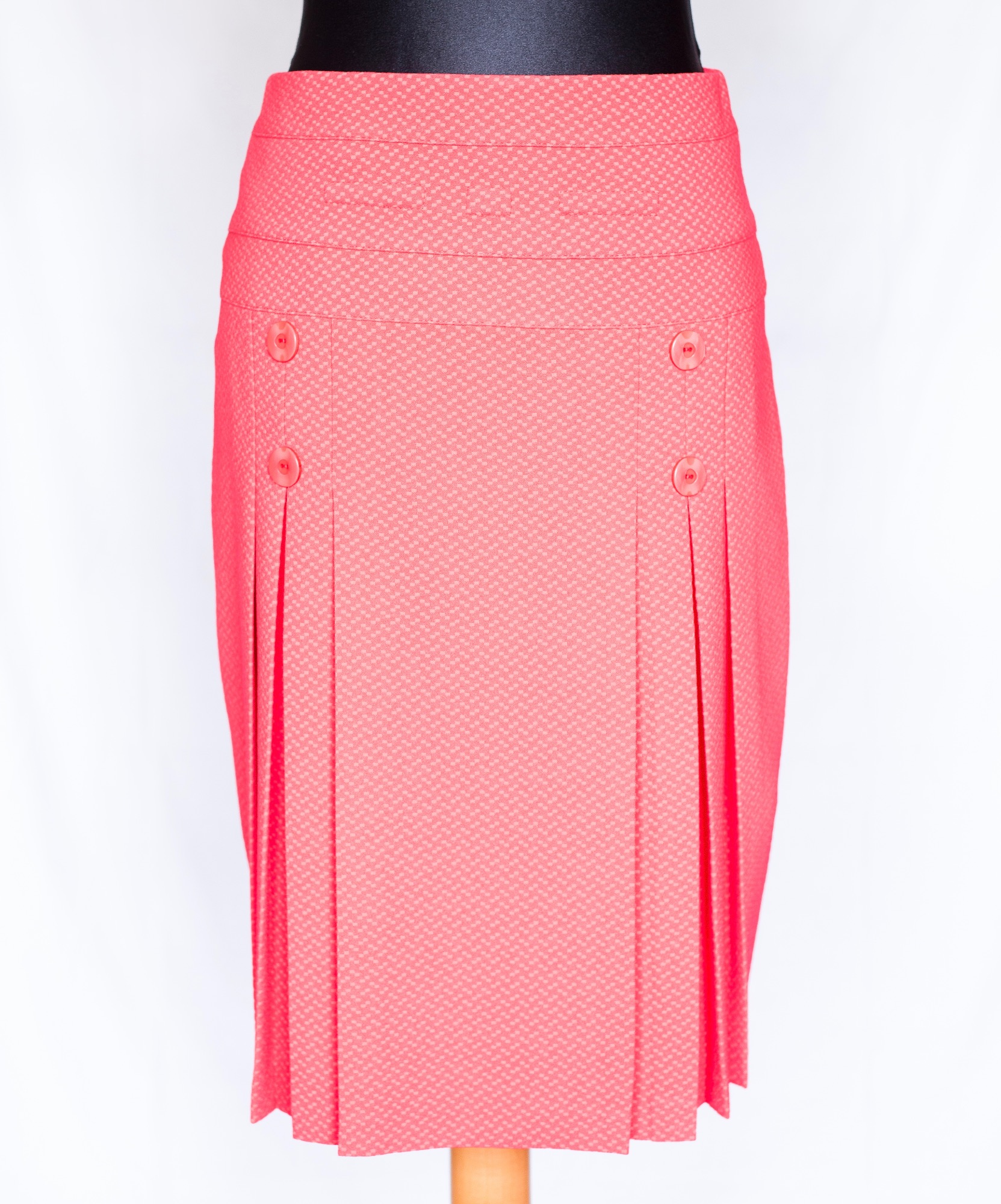 Koralowa spódnica ołówkowa z plisami i ozdobnymi guzikami, prezentowana na manekinie na białym tle.
