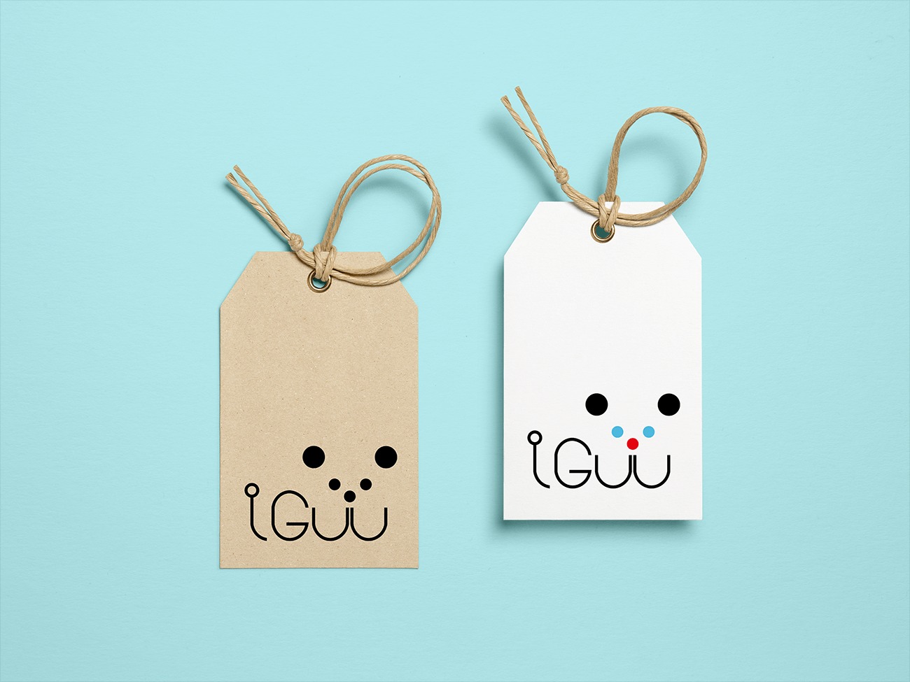 Dwie zawieszki z minimalistycznym logo na błękitnym tle. Jedna zawieszka jest z brązowego papieru, a druga biała. Logo przedstawia stylizowaną twarz z dwoma czarnymi kropkami jako oczami i napisem...