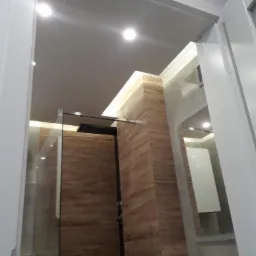 Nowoczesna kabina prysznicowa z drewnopodobnymi płytkami, oświetleniem LED i szklanymi drzwiami, widok z dołu przez otwarte drzwi.