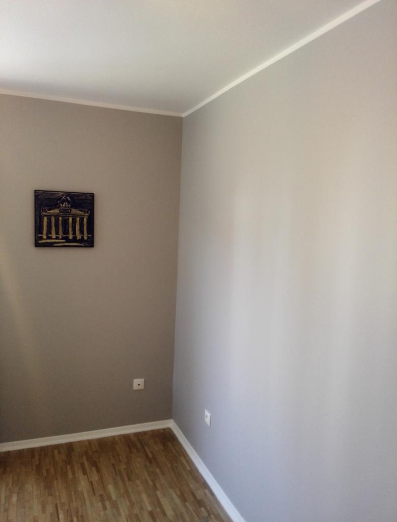 Pokój po remoncie: ściany pomalowane na dwa odcienie szarości, drewniana podłoga, białe listwy przypodłogowe i sufitowe, na ścianie obrazek przedstawiający budynek z kolumnami.