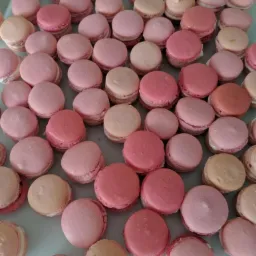 Różowe i beżowe makaroniki ułożone na jasnym blacie, widoczne delikatne kremowe nadzienie.