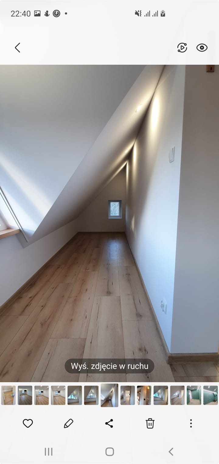 Poddasze po remoncie z drewnopodobną podłogą, skośną ścianą z oknem i oświetleniem LED wzdłuż krawędzi ściany.