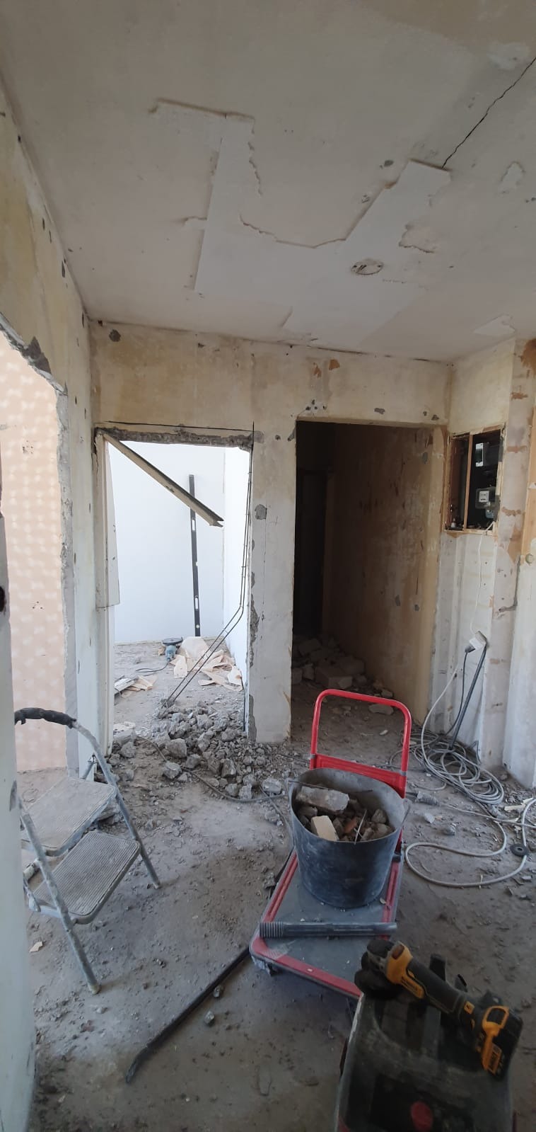 Demontaż starej instalacji elektrycznej i skuwanie tynku w trakcie remontu mieszkania, widoczny kubeł z gruzem, drabina i narzędzia.